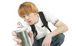 A teenage boy pointing a spray paint can directly at the camera lens.