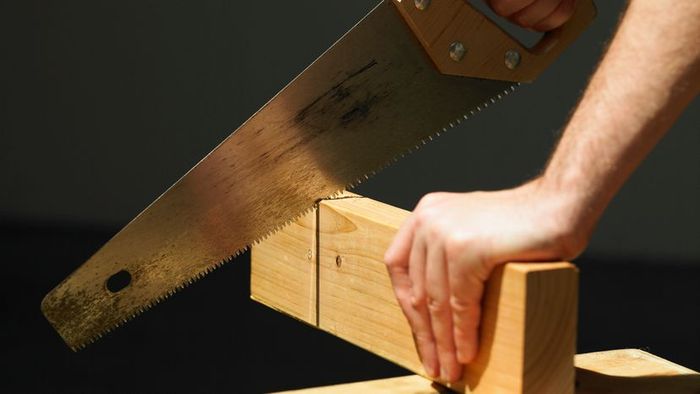 A person using a saw to slice through a wooden board.