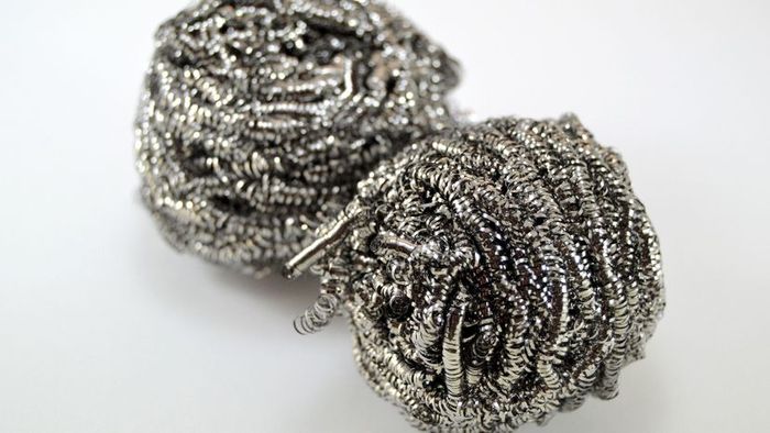 A close-up image of a metal scourer on a white background used for cleaning.