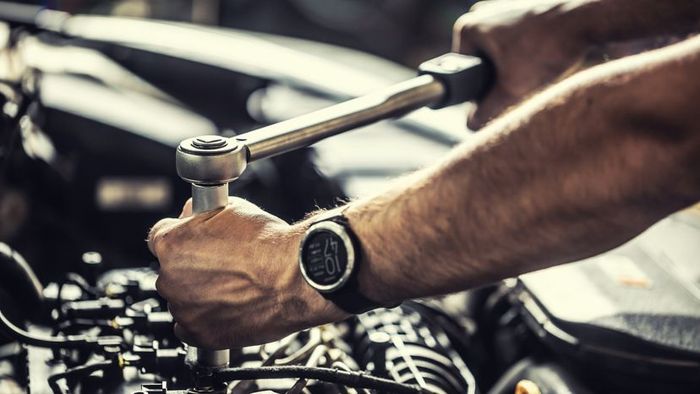 A mechanic using a torque wrench to repair a malfunctioning car engine.