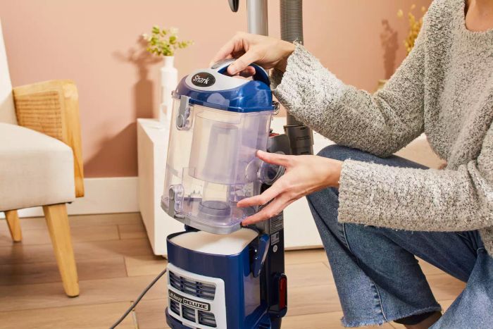 Person removing the canister Shark NV360 Navigator Lift-Away Deluxe Upright Vacuum displayed on a hardwood floor