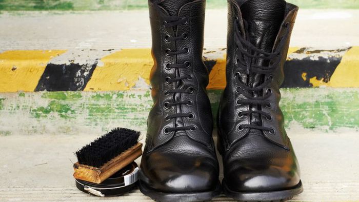 A pair of shiny black leather lace-up boots placed beside a shoe brush and a tin of polish.