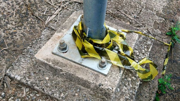 The base of a light pole, secured to the ground using screws.