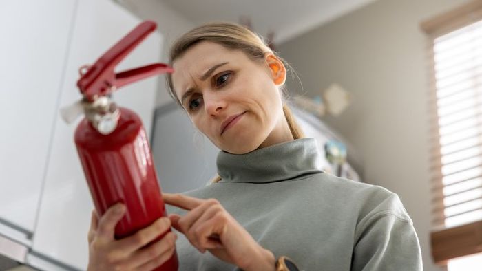 A woman checks the expiration date on a fire extinguisher at her home.