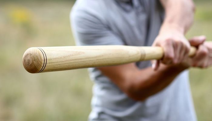 A close-up of a person taking a swing with a wooden baseball bat.