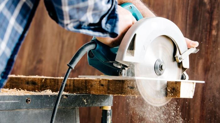 A male carpenter operating a circular saw in his home workshop.