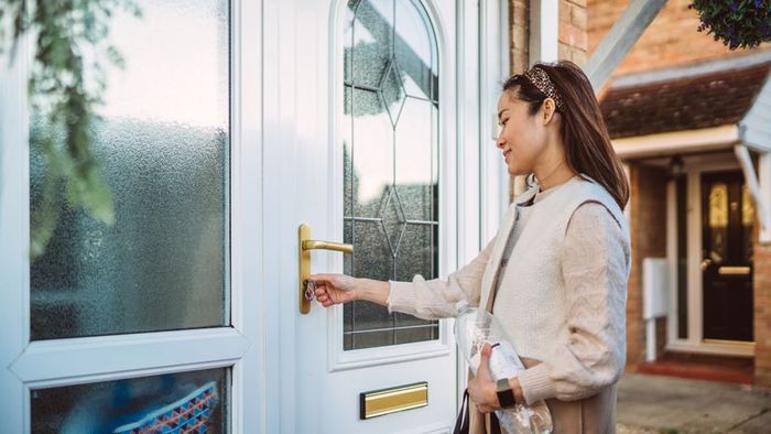 A young woman holds a water bottle as she unlocks her front door.
