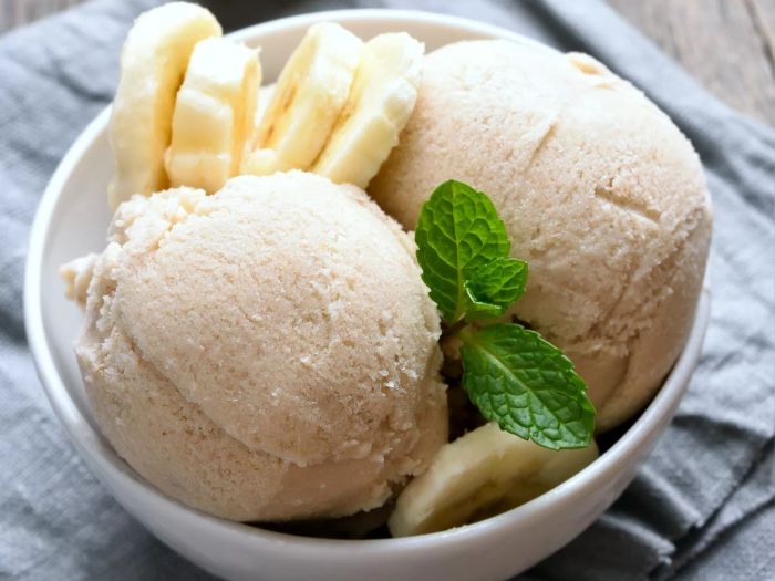 Two scoops of banana ice cream in a white bowl, garnished with sliced banana and a sprig of mint