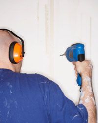 A person operating a drill while wearing earplugs