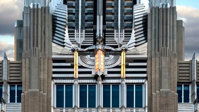 A striking stainless steel Art Deco winged sculpture graces the facade of an ornate building.