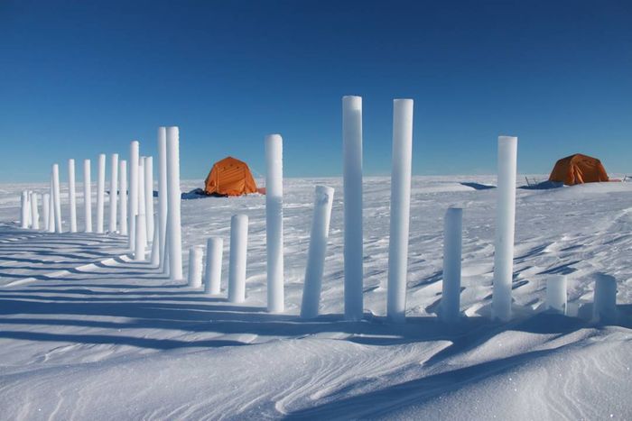 A view of the Greenland ice sheet showing ice cores being drilled alongside two orange tents.