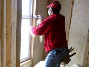 A construction worker applies insulation to a window in a newly built home