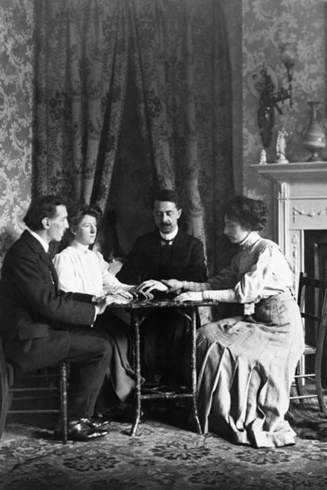 Two men and two women sit around a table during a seance.