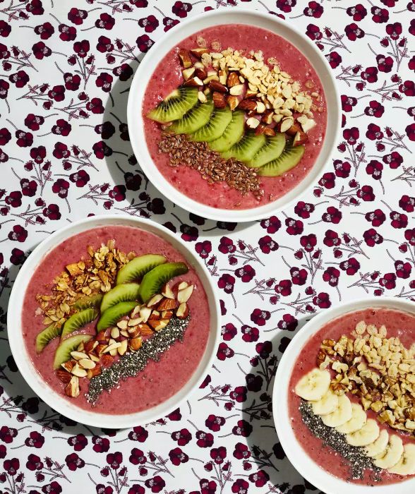 Three raspberry smoothie bowls arranged on a floral-patterned tablecloth.