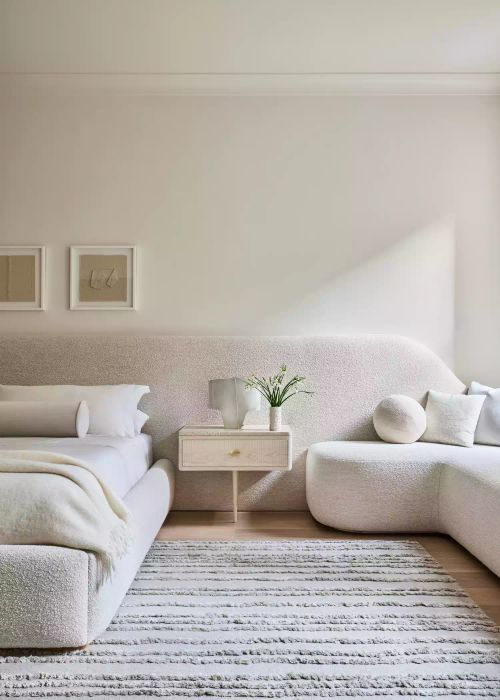 All-white bedroom with a curved bouclé bench, bed frame, and headboard
