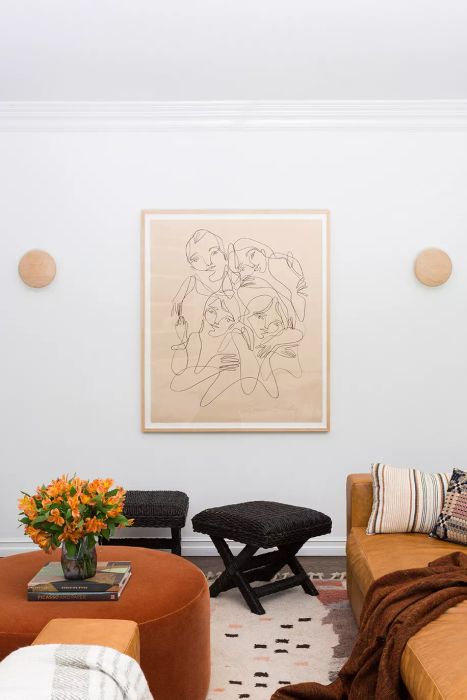 Living room featuring a leather sofa, orange ottoman, and line art of women