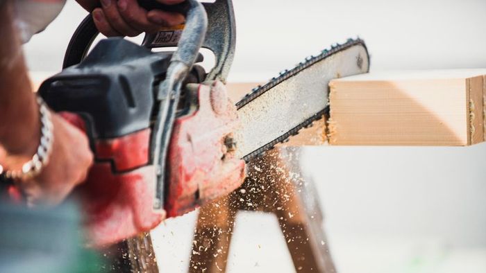 A close-up shot of a person cutting through a wooden beam using a chainsaw.