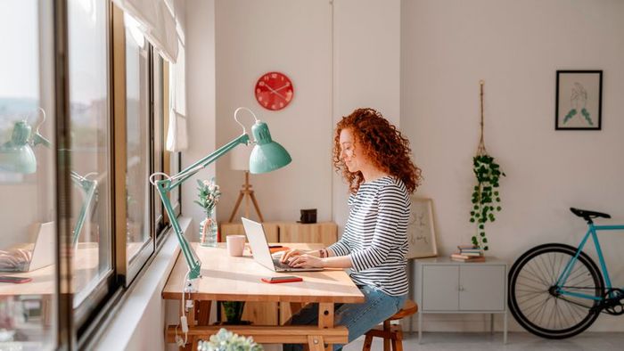 A woman working from home, seated at a desk with a laptop in use.