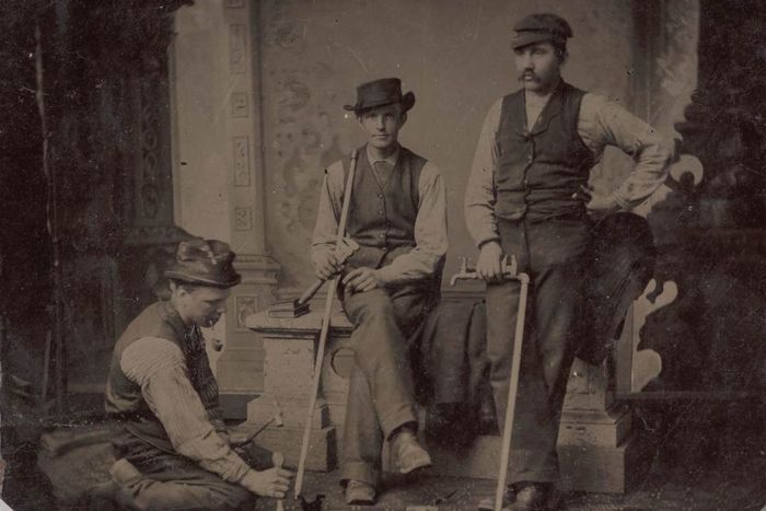 A trio of plumbers, each holding pipes and tools, ready to work.