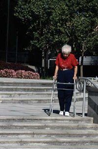 An elderly woman using a walker attempts to carefully descend a staircase.