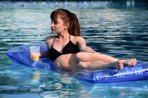 A young woman floats leisurely in a pool, sipping a drink while lounging on a swimming float.