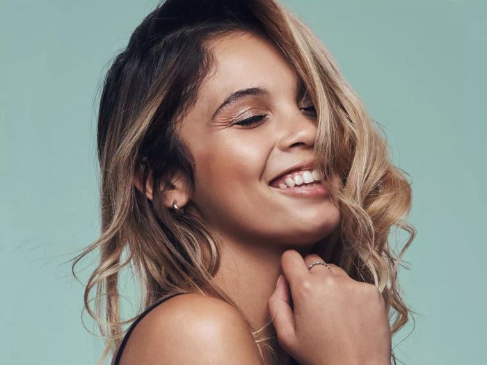 A brunette woman showcasing caramel highlights, flashing a smile