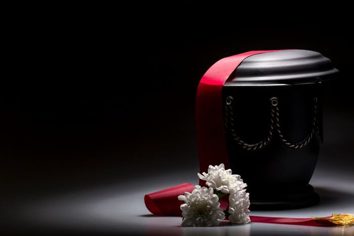 A black funerary urn and a white flower with red ribbons