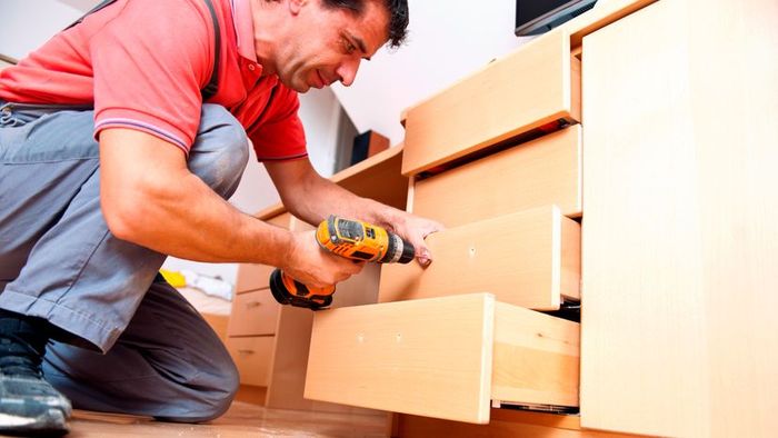 A person using tools to assemble a wooden drawer.