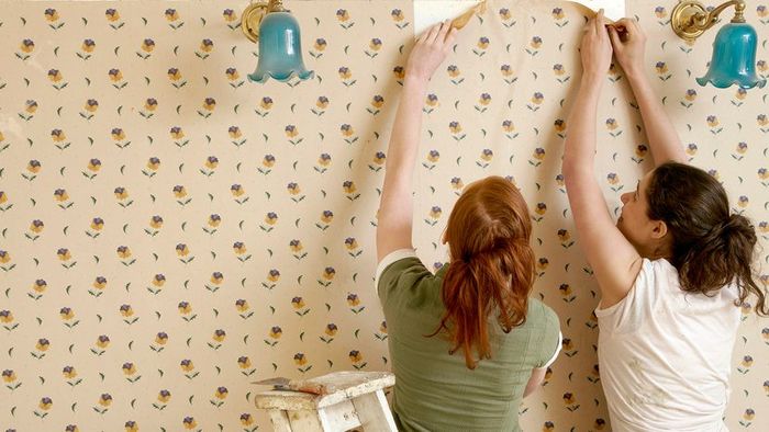 two individuals removing wallpaper from a wall