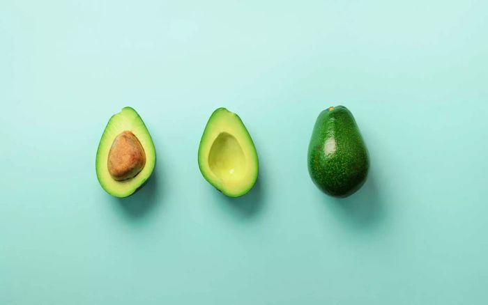 Organic avocado with seed, avocado halves, and whole fruits arranged on a blue background. A pop art-inspired design showcasing green avocados in a minimalist flat lay style.