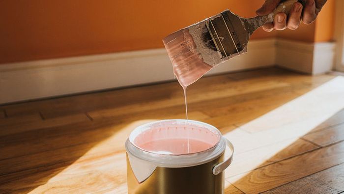 A hand firmly gripping a thick paintbrush, dripping with paint.