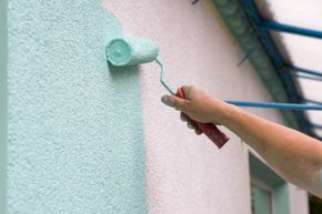 Applying paint to stucco with a roller.