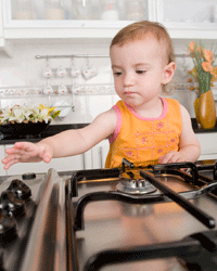 A child reaching for the knob of a gas stovetop
