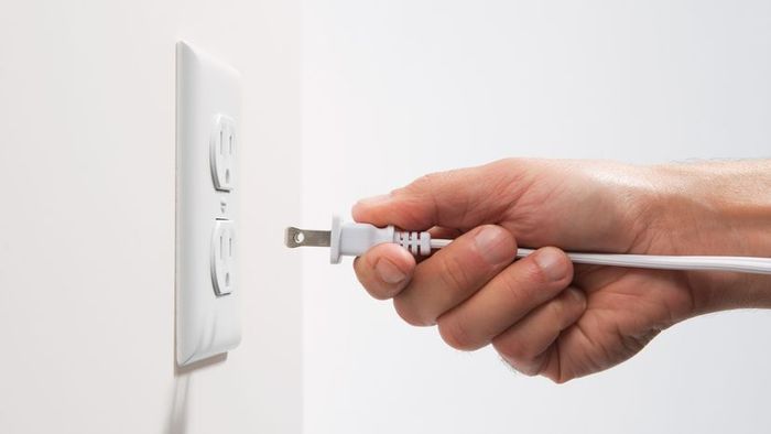 A person's hand inserting a plug into an electrical socket.