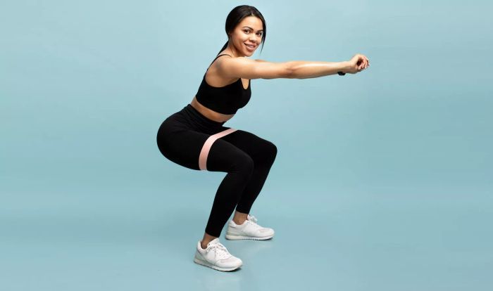 Strength training exercise. Woman performing squats with a resistance band in front of a blue background.