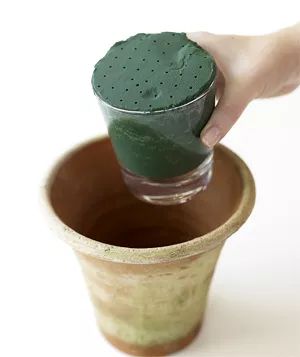 A glass filled with floral foam is being placed inside a terra-cotta pot