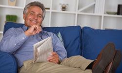 Man sitting on couch, reading newspaper