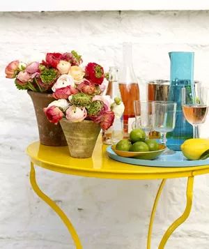 A terra cotta pot featuring a ranunculus flower arrangement set on a yellow table