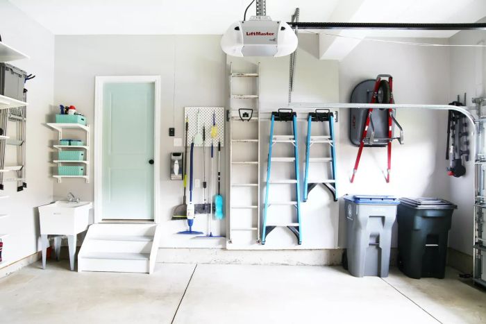 Garage with sleek gray walls, mint-colored door, wall-mounted ladders, organized pegboard for tools, and a neatly stored wheelbarrow