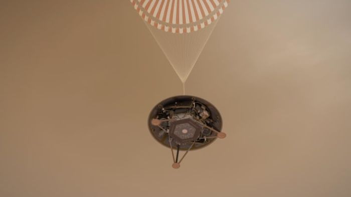 A visual representation of NASA's InSight lander descending towards Mars' surface under a parachute.