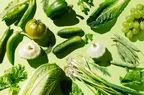 Fresh green organic vegetables and fruits arranged on a green background. A concept of healthy food, diet, and detox. A flat lay, top-down view.