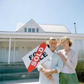 A group of individuals standing proudly in front of a house, holding a 'sold' sign