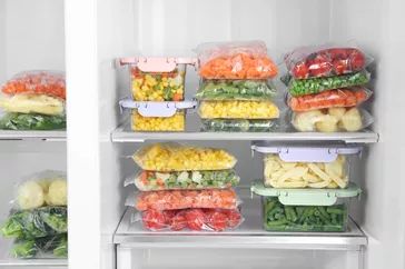 Plastic bags and containers filled with a variety of frozen vegetables in the refrigerator
