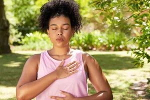 A woman dressed in athletic wear practicing breathing exercises during mindful meditation in a park