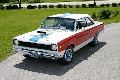 The 1969 AMC SC/Rambler, also known as the Scrambler, was a standout in the muscle car world. American Motors Corporation (AMC) teamed up with Hurst Performance to create this race-ready, production vehicle. The 'SC' in SC/Rambler stood for 'stock-car,' reflecting its racing pedigree. AMC installed a 390 cubic inch, 315 horsepower V8 engine into the lightweight Rambler Rogue hardtop coupe, staying true to the formula of putting a large engine into a small car. This muscle car was more than capable on the drag strip, regularly turning low 14-second quarter miles. With only one option available (an AM radio), the price was kept under $3,000. The interior was simple, featuring grey vinyl, bench seats, and red, white, and blue accents on the headrests, along with carpeting and a Borg-Warner 4-speed transmission with a Hurst shifter. The car's most eye-catching feature was its bold paint job, with the first 500 units sporting a white body and a wide red side panel, with a blue stripe running across the top. A functional 'Ram Air' induction scoop on the hood and blue two-toned mag wheels further set the SC/Rambler apart. After the first batch of 500 sold out, AMC released 500 more cars with a 'B' trim, and a third batch of 512 units, which may have returned to the 'A' trim, though this is debated by enthusiasts. Of the 1,512 SC/Ramblers produced, most of the surviving models today feature the 'A' trim. The SC/Rambler remains one of the lesser-known muscle cars of its time.