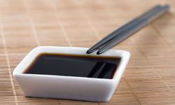 A small bowl of soy sauce rests on a bamboo mat, with two chopsticks leaning against the side.
