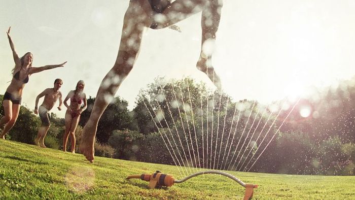 Young women in swimsuits enjoying themselves around a sprinkler.