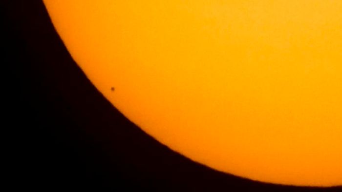 Mercury is shown in silhouette, positioned at the lower left of the image, as it transits across the Sun's face.