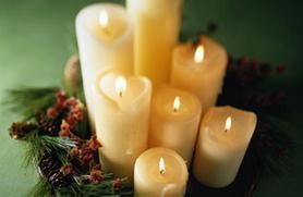 A collection of seven lit soy candles nestled within a wreath of greenery and pinecones.