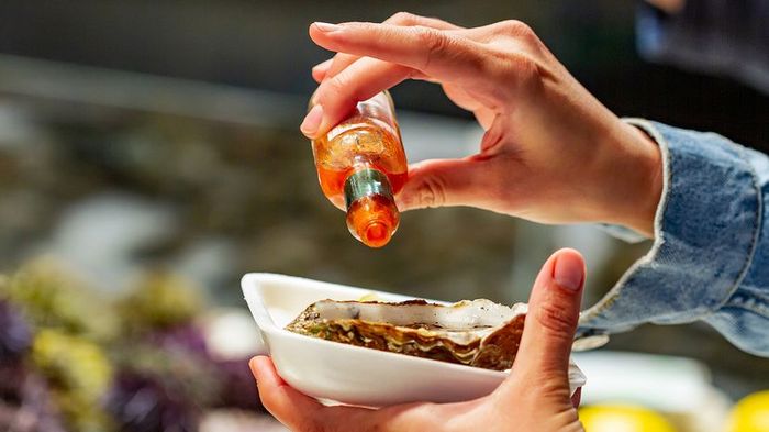 A person drizzles Tabasco sauce onto an oyster at the Paris Market in Bastille